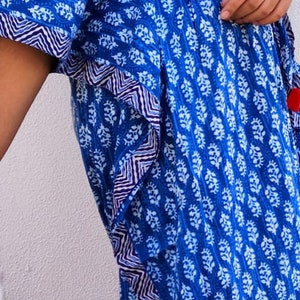 May include: A blue and white patterned kaftan with a V-neck and a tie at the waist. The kaftan has a white and blue trim around the edges.