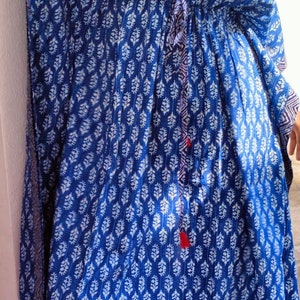 May include: A blue and white patterned kaftan with a drawstring waist and tassel tie. The kaftan has a V-neck and long sleeves.