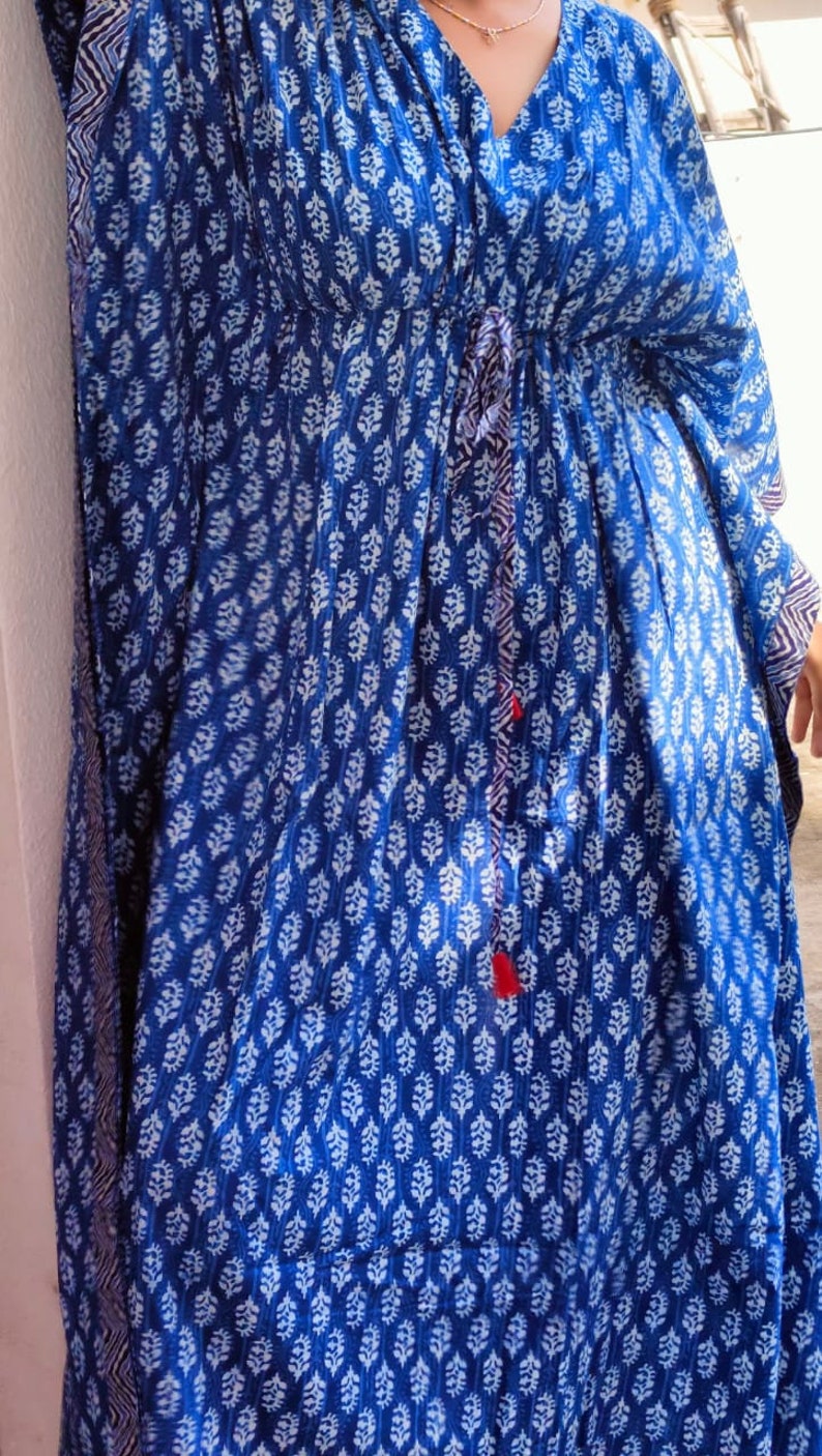 May include: A blue and white patterned kaftan with a drawstring waist and tassel tie. The kaftan has a V-neck and long sleeves.