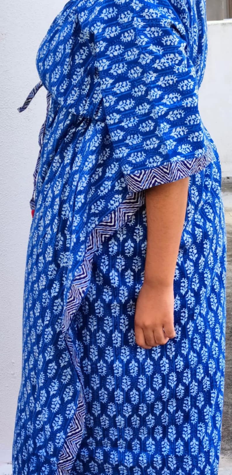 May include: A blue and white patterned dress with a tie at the waist. The dress has a loose fit and a flowing skirt.