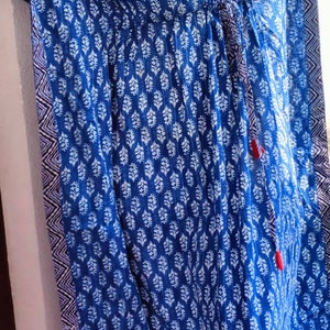May include: A blue and white patterned kaftan with a drawstring waist and tassel ties. The kaftan has a V-neck and is made of a lightweight fabric.