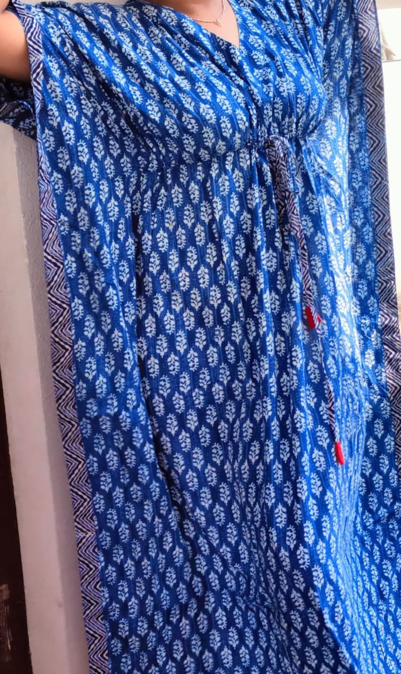 May include: A blue and white patterned kaftan with a drawstring waist and tassel ties. The kaftan has a V-neck and is made of a lightweight fabric.