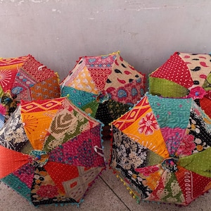 Puede incluir: Cinco paraguas de patchwork coloridos con patrones y texturas vibrantes. Cada paraguas presenta una combinación única de telas en tonos rojos, naranjas, verdes y azules. Los bordes están adornados con pequeños pompones decorativos.