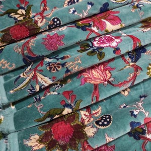 Puede incluir: Primer plano de tela turquesa con estampado floral. El dise&ntilde;o presenta grandes flores estilizadas en tonos rosa, rojo y crema, con follaje verde y azul. La tela est&aacute; doblada, mostrando su textura y los detalles del estampado.