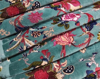 May include: Close-up of teal fabric with a floral pattern. The design features large, stylized flowers in shades of pink, red, and cream, with green and blue foliage. The fabric is folded, showing its texture and the intricate details of the print.