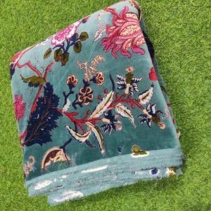 Puede incluir: Tela doblada de color verde azulado con un estampado floral en rosa, rojo y blanco. La tela tiene una textura suave y aterciopelada y est&aacute; doblada cuidadosamente. El dise&ntilde;o floral incluye hojas y otros elementos bot&aacute;nicos.
