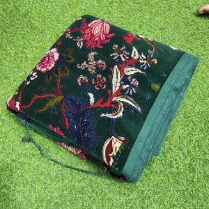 May include: Folded green fabric with a floral pattern in red, white, and blue. The fabric has a velvety texture and is folded neatly. The floral design includes various flower and leaf shapes.