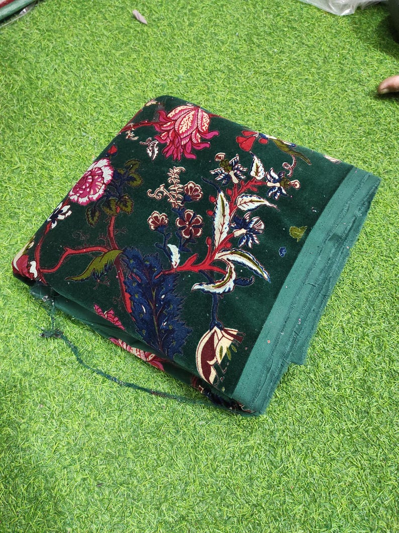 May include: Folded green fabric with a floral pattern in red, white, and blue. The fabric has a velvety texture and is folded neatly. The floral design includes various flower and leaf shapes.