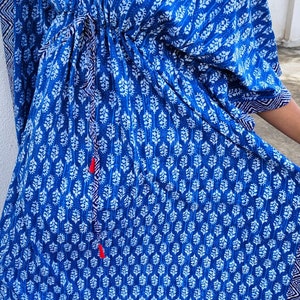 May include: A blue and white patterned kaftan with a drawstring waist and long sleeves. The kaftan has a V-neck and a white trim around the neckline and sleeves.