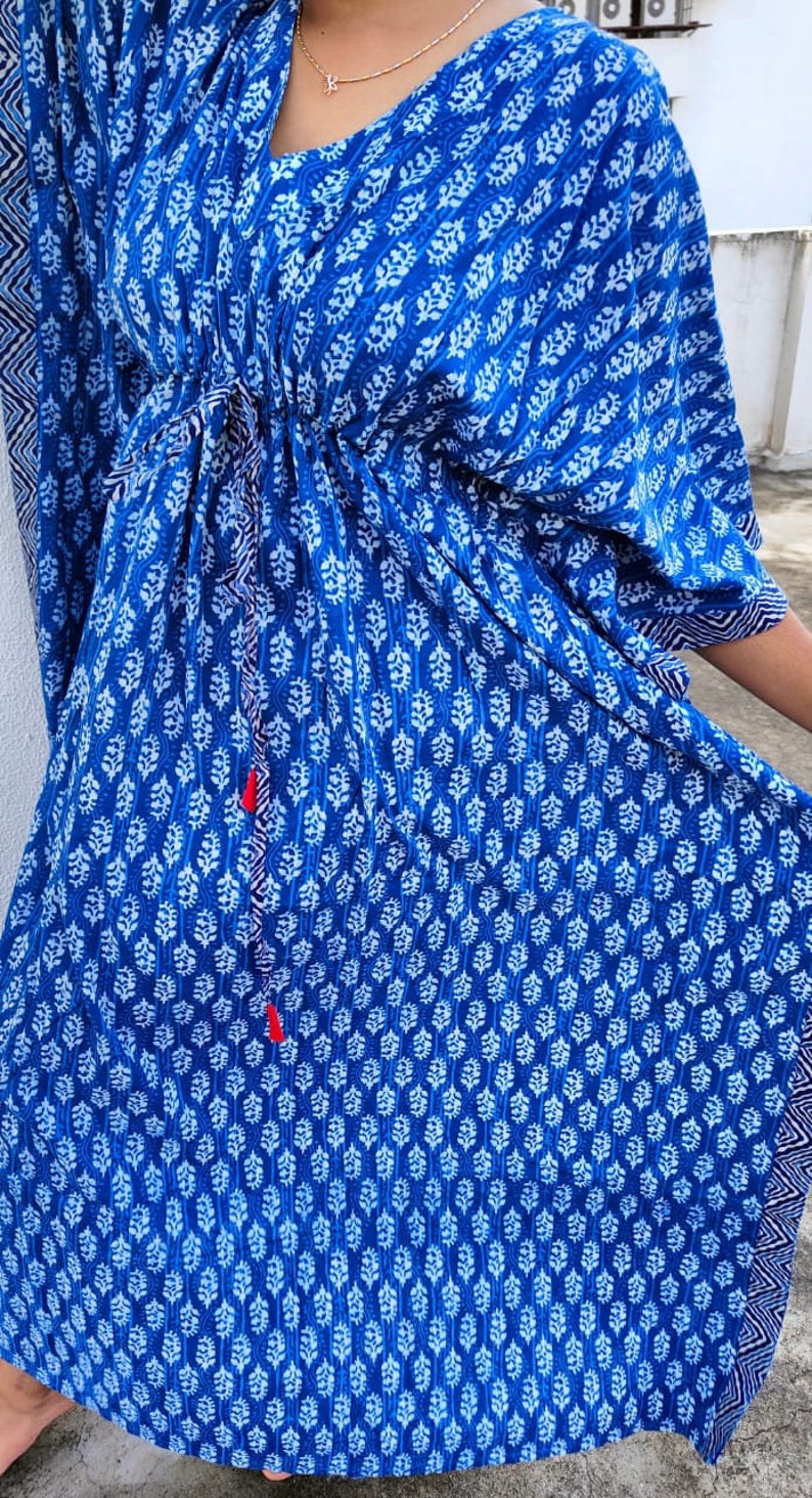 May include: A blue and white patterned kaftan with a drawstring waist and long sleeves. The kaftan has a V-neck and a white trim around the neckline and sleeves.