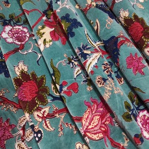 Puede incluir: Primer plano de tela de terciopelo turquesa con un estampado floral. El dise&ntilde;o presenta grandes flores estilizadas en tonos rojos, rosas y azules, con hojas verdes y tallos marrones. La tela est&aacute; doblada, mostrando profundidad y textura.