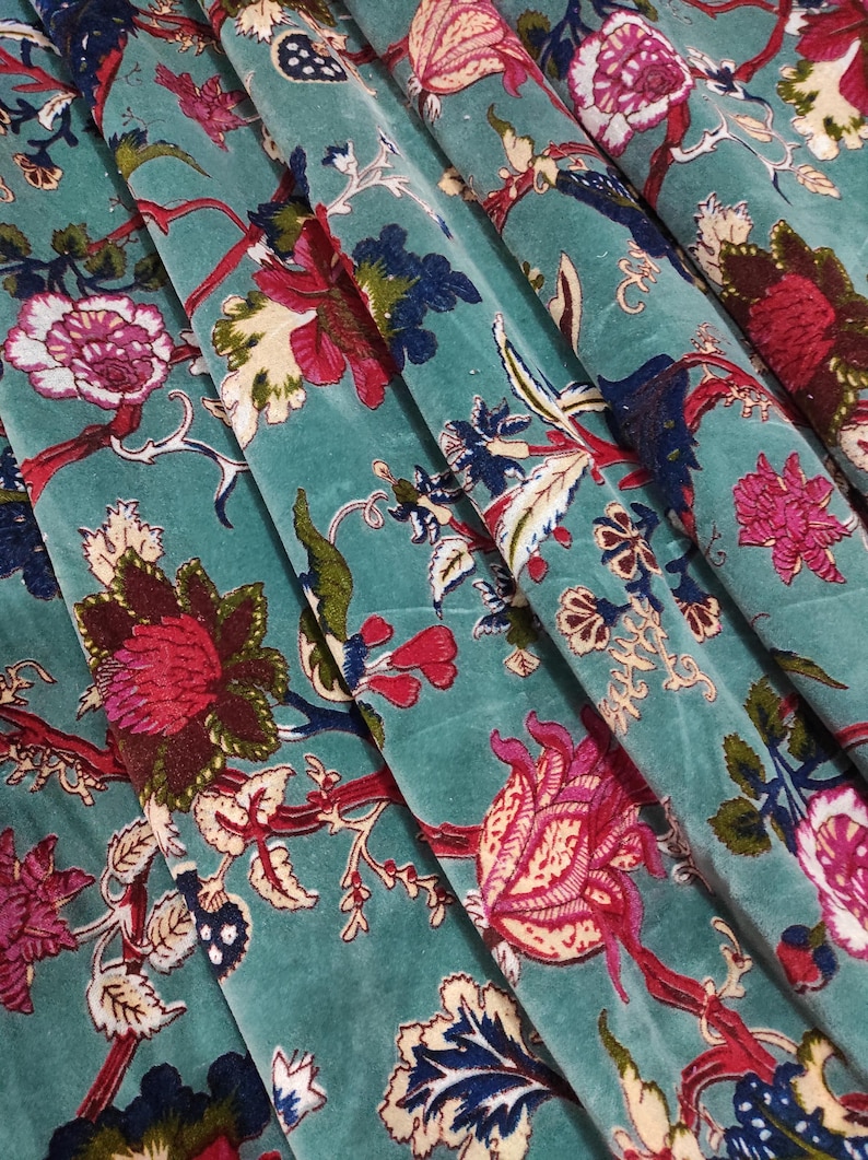 Puede incluir: Primer plano de tela de terciopelo turquesa con un estampado floral. El dise&ntilde;o presenta grandes flores estilizadas en tonos rojos, rosas y azules, con hojas verdes y tallos marrones. La tela est&aacute; doblada, mostrando profundidad y textura.