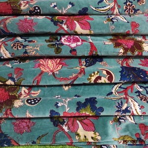 Puede incluir: Primer plano de tela apilada con fondo turquesa y estampado floral. El estampado presenta grandes flores rosas y rojas, hojas azules y detalles en crema. La tela est&aacute; doblada y apilada.