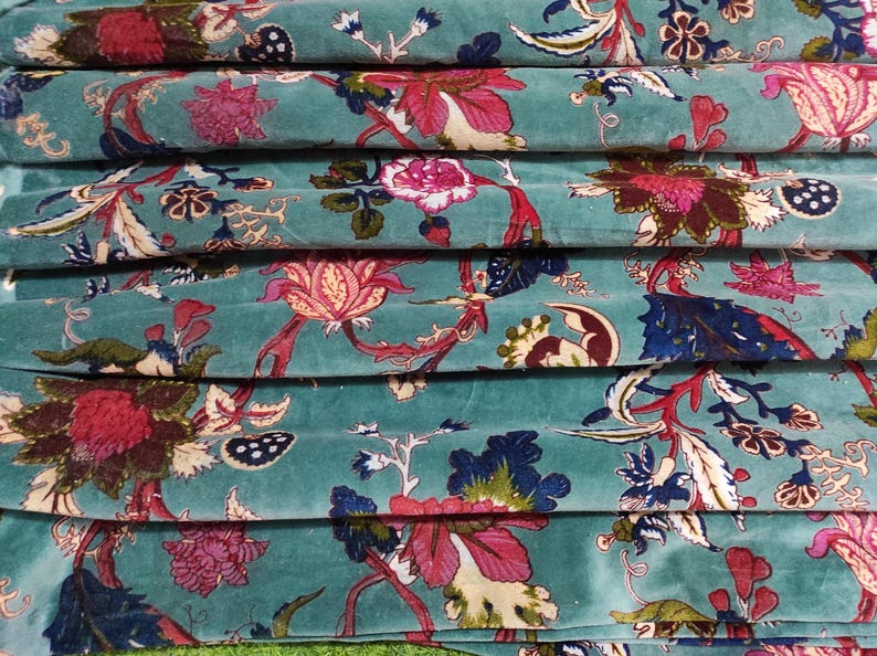Puede incluir: Primer plano de tela apilada con fondo turquesa y estampado floral. El estampado presenta grandes flores rosas y rojas, hojas azules y detalles en crema. La tela est&aacute; doblada y apilada.
