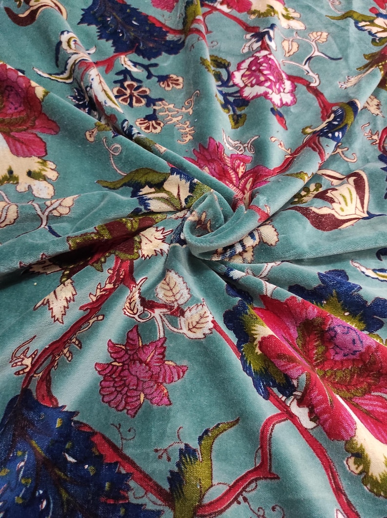 Puede incluir: Tela de terciopelo color turquesa con un estampado floral. El dise&ntilde;o presenta grandes flores estilizadas en tonos rosa, rojo y azul, sobre un fondo turquesa. La tela tiene un aspecto suave y lujoso, con pliegues y textura visibles.