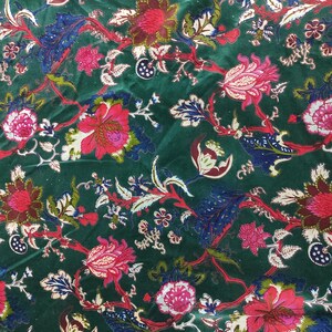 May include: A close-up of a dark green fabric with a floral pattern. The design features large, red and pink flowers with white and green accents, along with blue and white leaves. The fabric has a velvet-like texture.