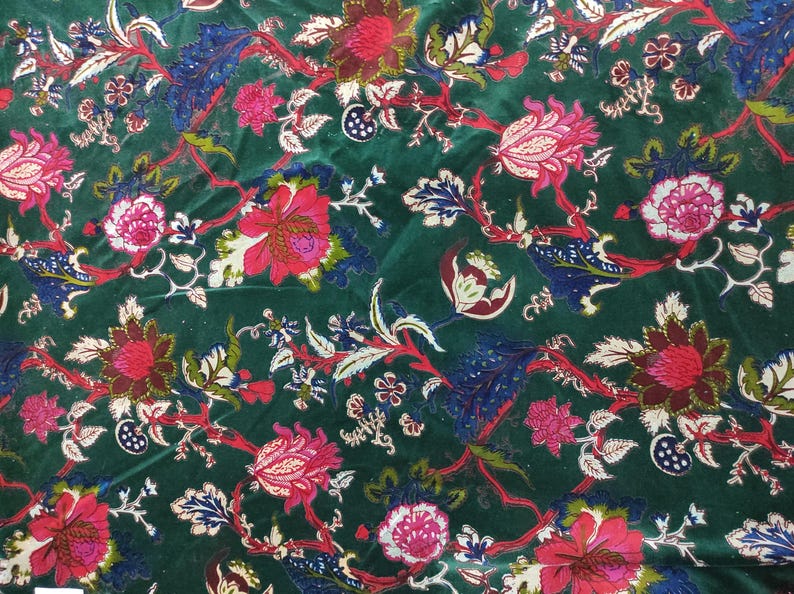 May include: A close-up of a dark green fabric with a floral pattern. The design features large, red and pink flowers with white and green accents, along with blue and white leaves. The fabric has a velvet-like texture.