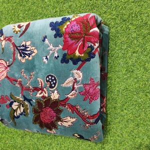 Puede incluir: Tela doblada de color turquesa con un estampado floral. El dise&ntilde;o presenta grandes flores vibrantes en tonos rosa y burdeos, con detalles en azul y blanco. Probablemente una manta o un cubrecama.