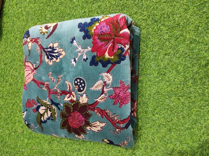 Puede incluir: Tela doblada de color turquesa con un estampado floral. El dise&ntilde;o presenta grandes flores vibrantes en tonos rosa y burdeos, con detalles en azul y blanco. Probablemente una manta o un cubrecama.