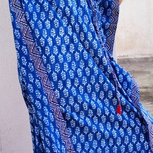 May include: A blue and white patterned kaftan with a red tassel. The kaftan has a V-neck and a long, flowing silhouette.