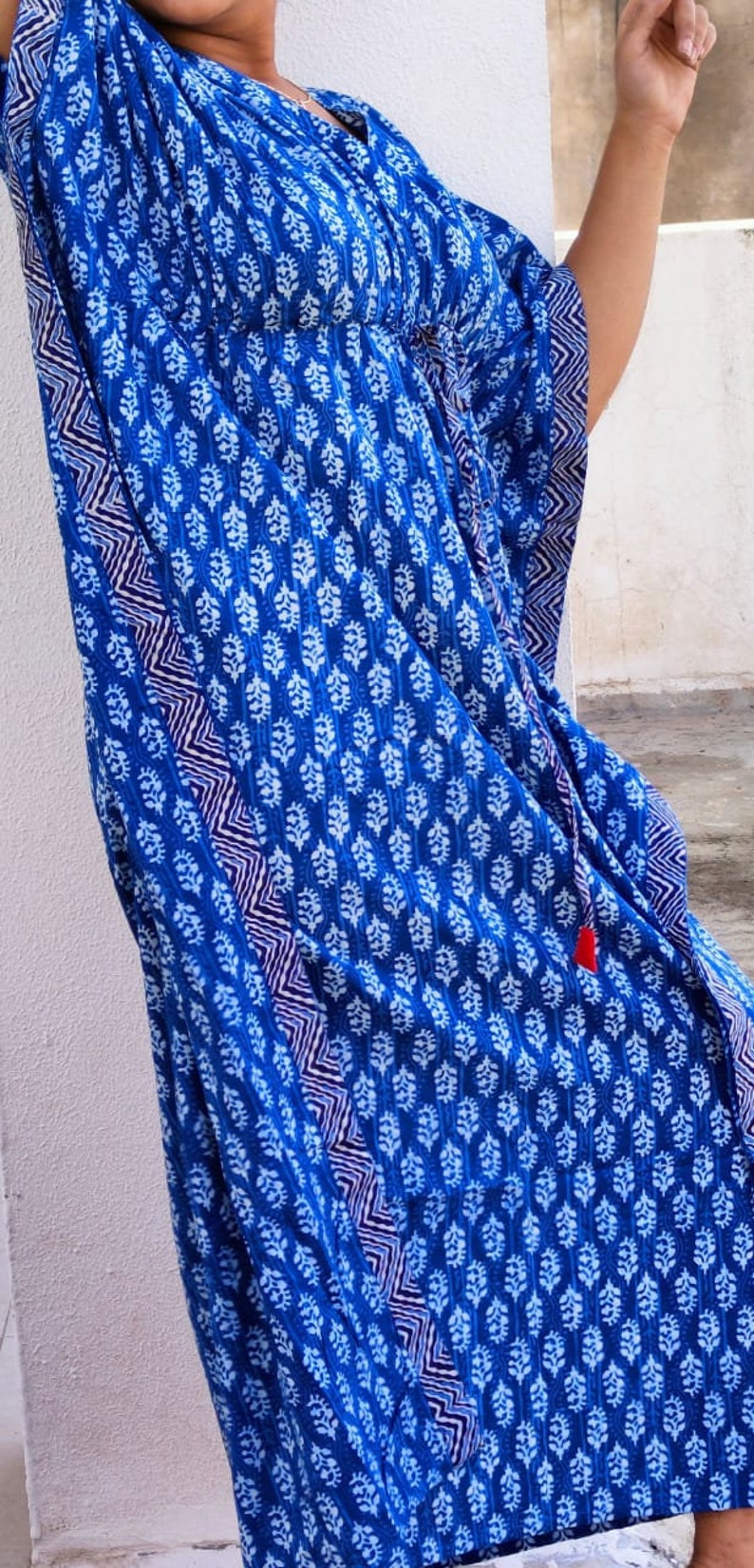May include: A blue and white patterned kaftan with a red tassel. The kaftan has a V-neck and a long, flowing silhouette.