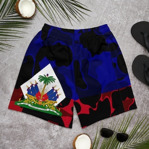 May include: Blue, red and black patterned swimming shorts with the Haitian flag on the left leg. The flag features a palm tree, cannons and the text "L'UNION FAIT LA FORCE".