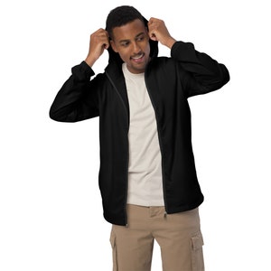 May include: A black hooded jacket with a full-length zip. The jacket is worn over a white t-shirt and paired with khaki cargo trousers. The person is adjusting the hood of the jacket.