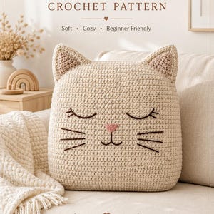 Puede incluir: Un cojín de gato tejido a ganchillo en color beige con orejas puntiagudas, ojos cerrados bordados, nariz rosa y bigotes marrones. El texto dice: CAT PILLOW CROCHET PATTERN, Soft, Cozy, Beginner Friendly, STEP-BY-STEP PATTERN, BabyPurl Co COZY HOME CROCHET COLLECTION.