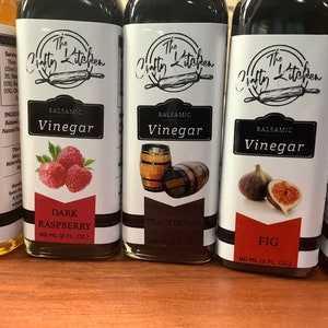 May include: Four glass bottles of balsamic vinegar with labels featuring the text "The Crafty Kitchen". The flavors are Fresh Peach, Dark Raspberry, Traditional, and Fig. Each bottle contains 60 ml (2 fl oz) of vinegar.
