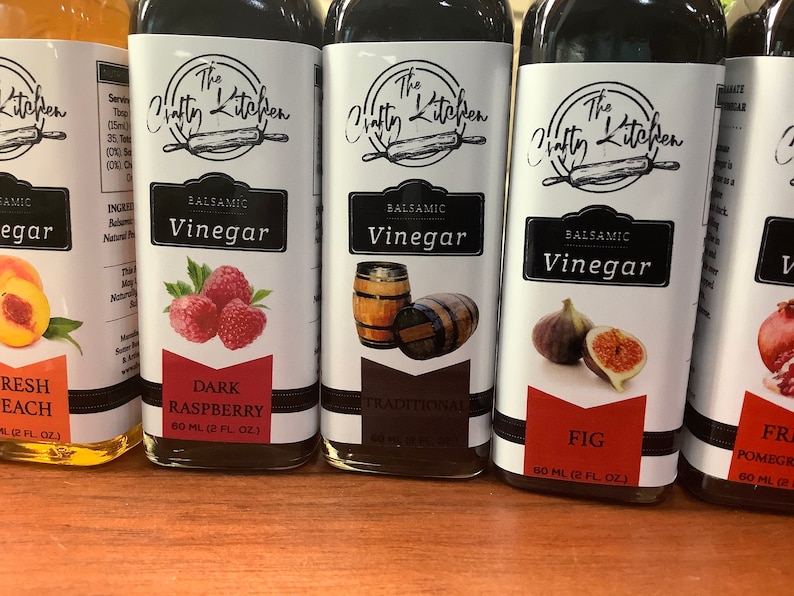 May include: Four glass bottles of balsamic vinegar with labels featuring the text "The Crafty Kitchen". The flavors are Fresh Peach, Dark Raspberry, Traditional, and Fig. Each bottle contains 60 ml (2 fl oz) of vinegar.