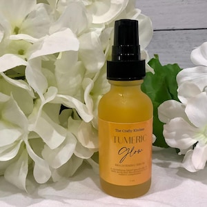 Puede incluir: Una botella de vidrio amarillo con una tapa de bomba negra, etiquetada como "Tumeric Glow Brightening Serum", se encuentra frente a flores blancas. La botella est&aacute; rodeada de flores blancas y hojas verdes.