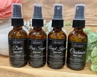 Puede incluir: Cuatro botellas de vidrio ámbar con etiquetas negras y pulverizadores. Las etiquetas dicen "The Crafty Kitchen" y presentan diferentes aromas: "Diva Body Mist", "Pink Sugar Body Mist", "Angel Kiss Body Mist" y "Cashmere Body Mist".