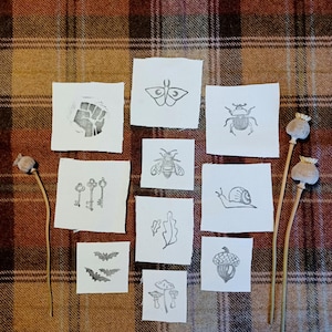 May include: A set of 12 small, white, square cards with black ink illustrations. The illustrations include a moth, a beetle, a bee, a snail, a leaf, an acorn, a mushroom, a bat, keys, and a fist.