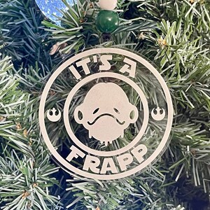 May include: A clear round Christmas ornament with a white outline of a character from Star Wars, the text "It's a Frapp" and the Rebel Alliance symbol.