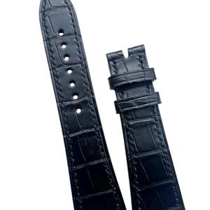 May include: Two-piece black watch strap made of textured leather. The strap has a crocodile skin pattern and is stitched along the edges. The strap has multiple holes for adjustment and a buckle closure.