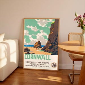 May include: A framed vintage travel poster for Cornwall, featuring a beach scene with cliffs, ocean, and sky. The poster has text that reads "Cornwall" and "Monthly Return Tickets - Penny A Mile - Issued All The Year Round."