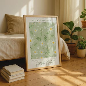 May include: A framed wall art print featuring a sage green background with a repeating pattern of white daisies and green leaves. The text FLOWER MARKET is at the top, and the text COLLECTION Portobello Market NO. 09 is at the bottom.