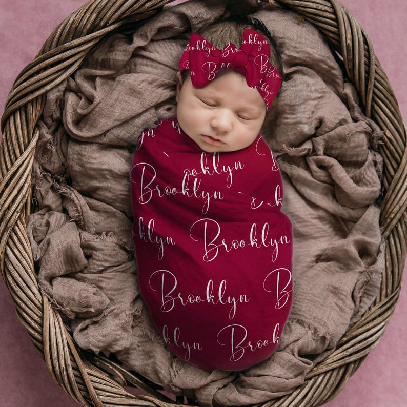 Pode incluir: Um rec&eacute;m-nascido envolto em um cobertor e faixa de cabelo bord&ocirc; combinando, ambos adornados com o nome "Brooklyn" em uma escrita delicada. O beb&ecirc; descansa pacificamente em uma cesta de vime forrada com tecido macio de tons neutros.