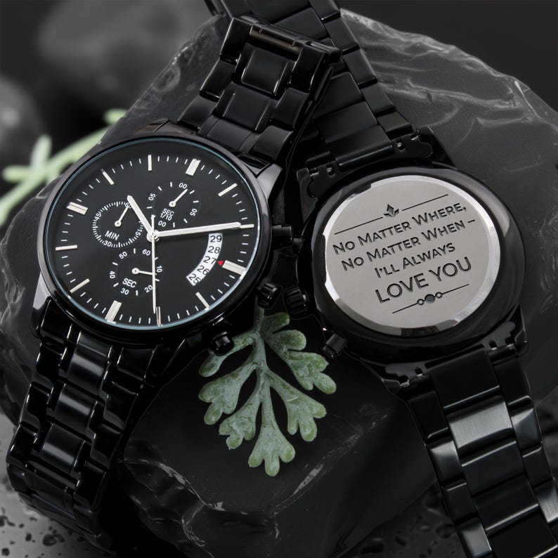 May include: Two black watches with matching bands. One watch face displays the time with multiple sub-dials and a date window. The other watch has the inscription "No Matter Where, No Matter When - I'll Always Love You."