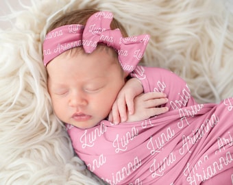 May include: A pink swaddle blanket with the names "Luna" and "Arianna" written in white script. A baby girl is sleeping in the swaddle, wearing a pink headband with the same names written on it.