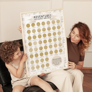 Op de afbeelding: Een ingelijste poster met een witte achtergrond en gouden cirkels. De cirkels bevatten tekst met activiteiten die een moeder en kind samen kunnen doen. De tekst luidt "Adventures for Mummy and Nola". De poster is versierd met bloemillustraties.
