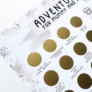 Op de afbeelding: Een printbare gouden en witte kaart met de tekst "Adventures for Mummy and Me" en een lijst met activiteiten om samen te doen, zoals "Dagje naar het strand", "Zelfgemaakte pizza", "Pannenkoeken bakken", "Bezoek aan een aquarium", "Verstoppertje spelen", "Huisdisco", "Rommelig spelen" en "Zwemmen met de mosselen".