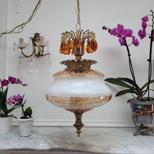 May include: A vintage brass and glass chandelier with a white and gold iridescent glass shade. The chandelier has a chain and a cluster of amber glass crystals.