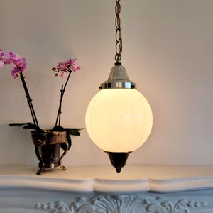 May include: A white frosted glass globe pendant light fixture with a silver chain and a silver and brass ceiling mount. The light is hanging above a white mantel with ornate carvings.