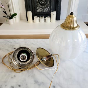 May include: A disassembled white glass globe pendant light fixture with a brass chain and a brass ceiling mount. The fixture has a white frosted glass globe and a brass finial.