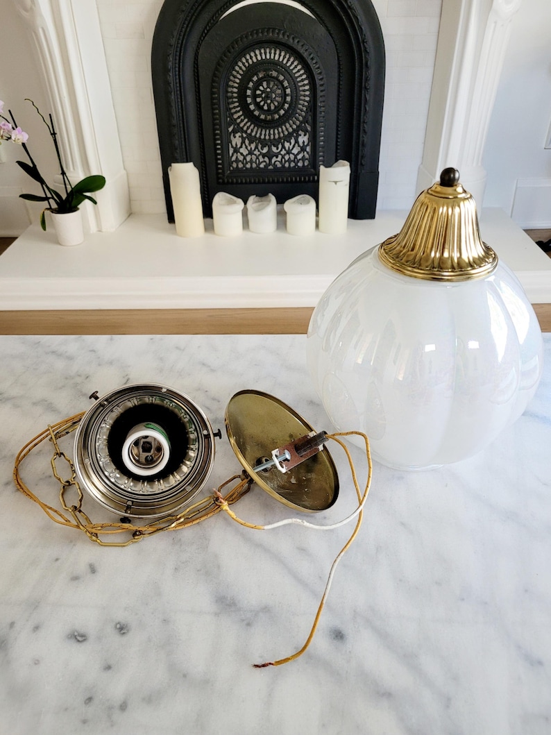 May include: A disassembled white glass globe pendant light fixture with a brass chain and a brass ceiling mount. The fixture has a white frosted glass globe and a brass finial.