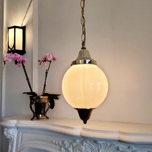 May include: A white globe pendant light fixture with a gold chain and a white ceiling mount. The light is on and illuminating the room.