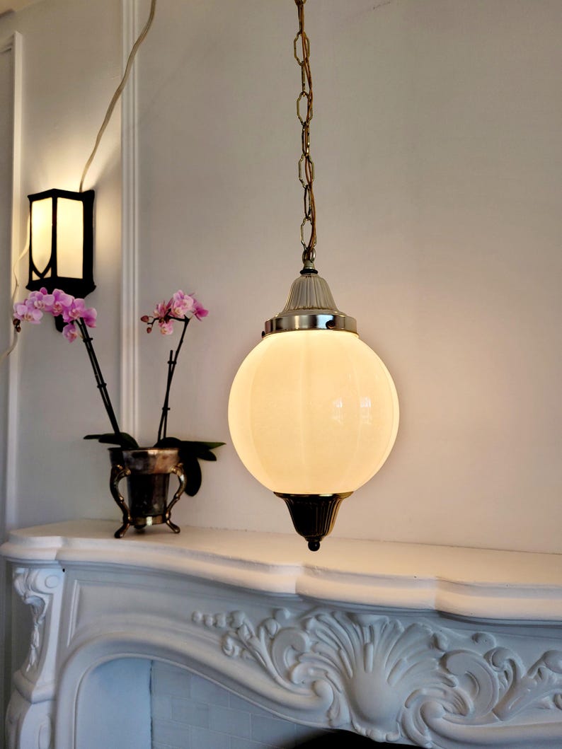 May include: A white globe pendant light fixture with a gold chain and a white ceiling mount. The light is on and illuminating the room.