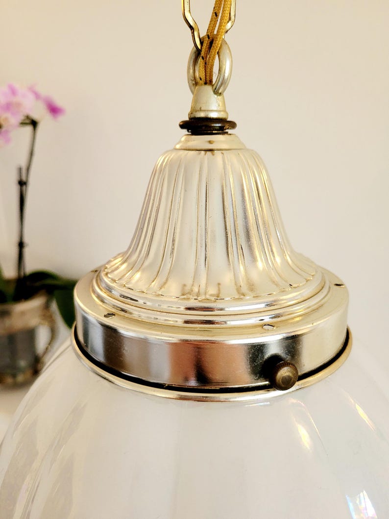 May include: A white glass globe pendant light fixture with a silver metal top and a decorative fluted design. The fixture is hanging from a chain.