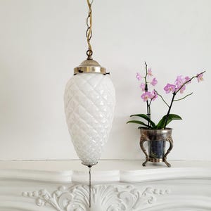 May include: A white glass pendant light fixture with a diamond pattern hangs from a chain. The light fixture is suspended above a white fireplace mantel with ornate detailing.